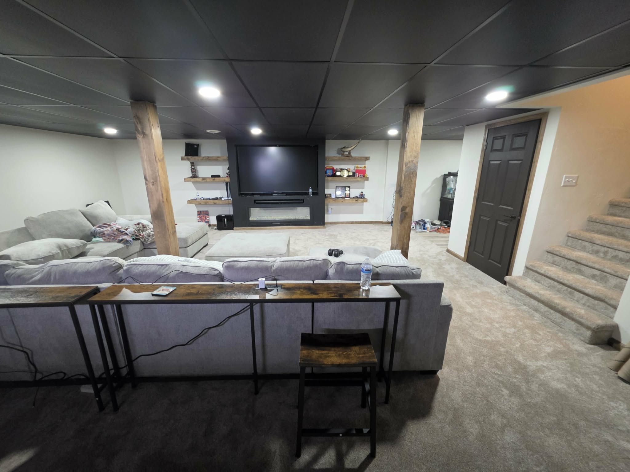 Completed basement living area with sectional seating, bar seating, entertainment wall, finished stairs, and coordinated flooring and lighting