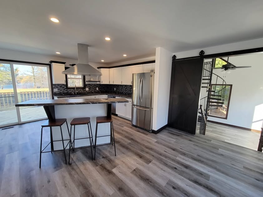Open remodeled kitchen and living area with white cabinetry, dark accents, a barn door, and spiral staircase